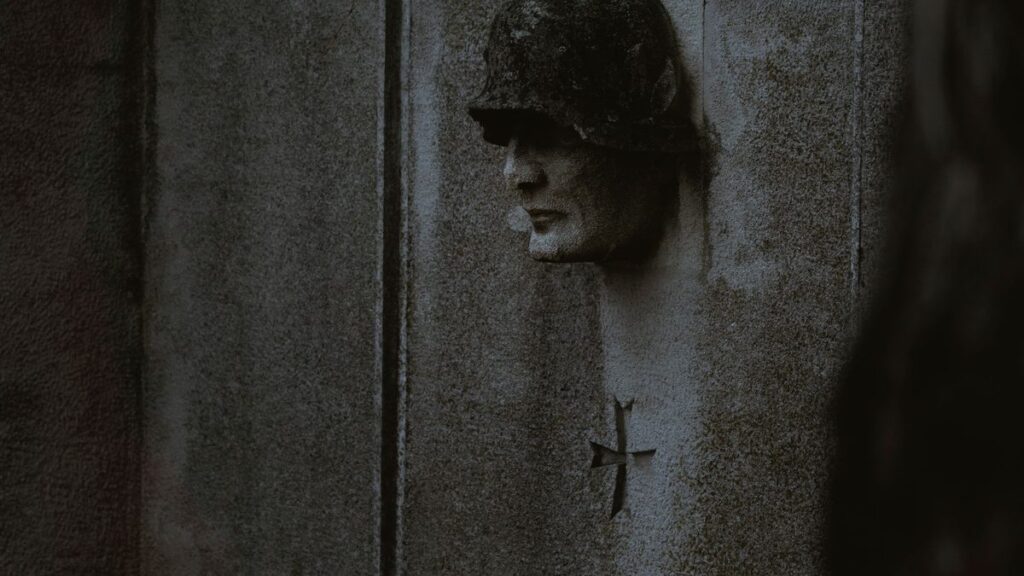 Dark concrete wall with a soldier sculpture and a cross symbol.