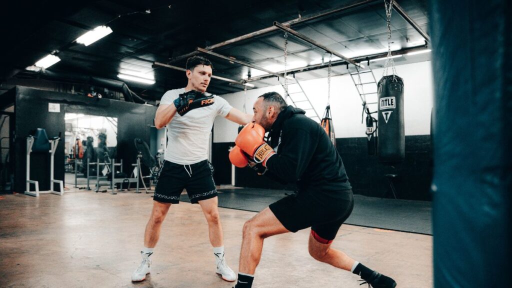 Two men engaged in a dynamic boxing training session indoors, showcasing fitness and athleticism.