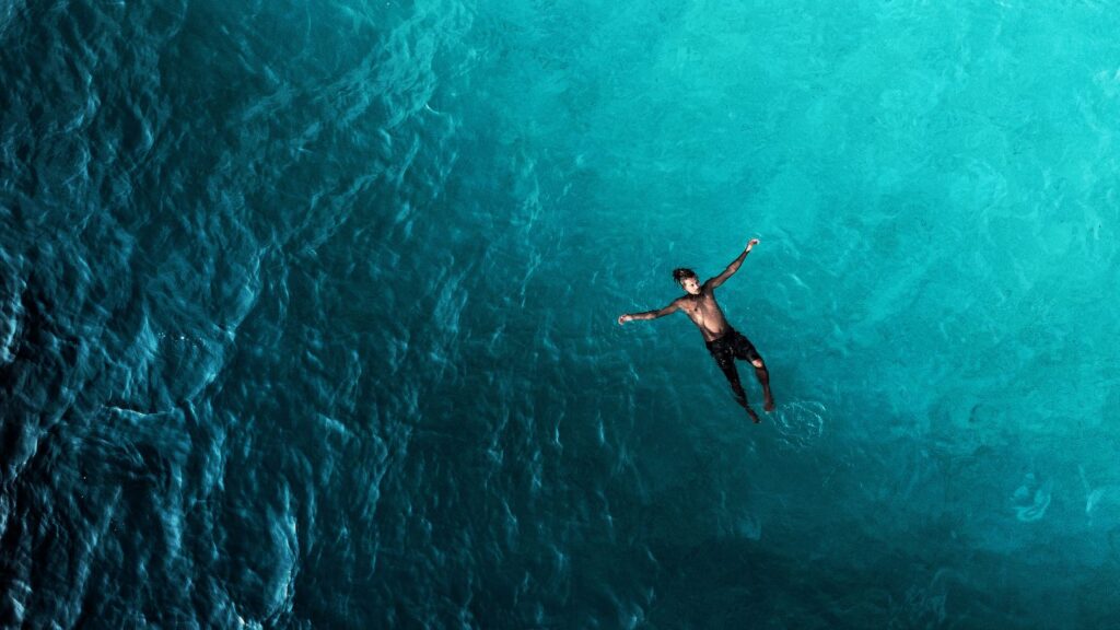 Lone swimmer floating in deep turquoise open water seen from above