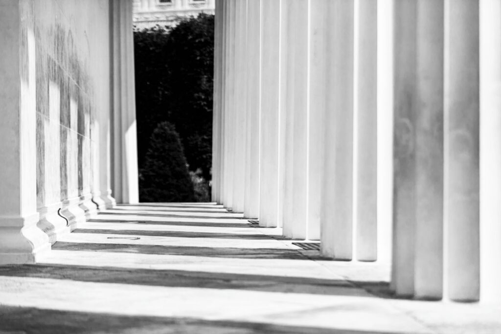Row of white classical columns casting long shadows in black and white
