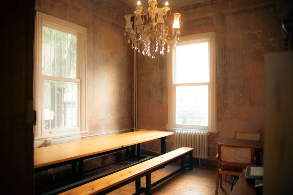 Long wooden table and benches in an old room with tall windows and a chandelier